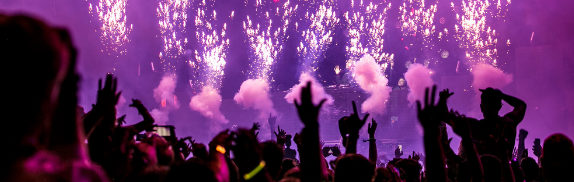 Público com as mãos erguidas em show ao ar livre com fogos