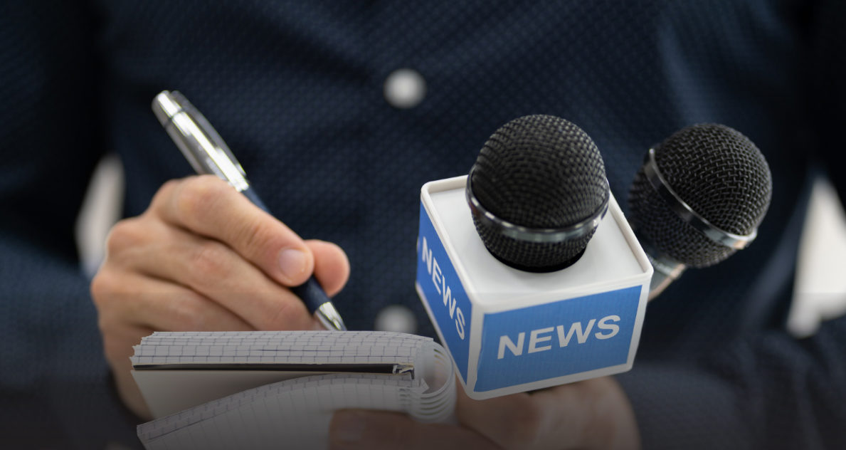 Repórter anota declarações durante entrevista coletiva, com microfones à frente